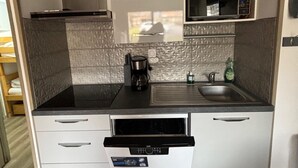 Une cuisine compacte dotée d’un plan de travail noir, d’une machine à café, d’un évier et d’un four à micro-ondes. Les armoires sont blanches et le pare-feu est texturé.