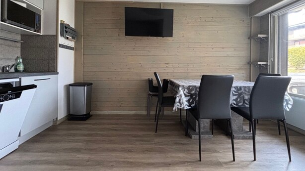 Une cuisine moderne avec un coin repas, un téléviseur à écran plat fixé au mur et une vue sur l’extérieur grâce à une grande fenêtre.