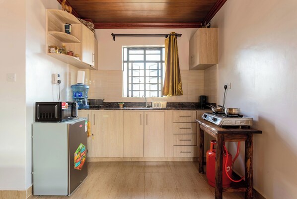 A compact kitchen with a refrigerator, microwave, gas stove, and a window with a curtain.