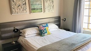 Un lit avec une literie blanche, un coussin coloré, une tête de lit et trois œuvres d’art murales.