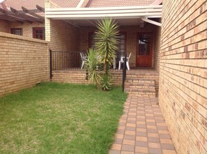 A brick house with a paved patio, a small lawn, and a metal gate.