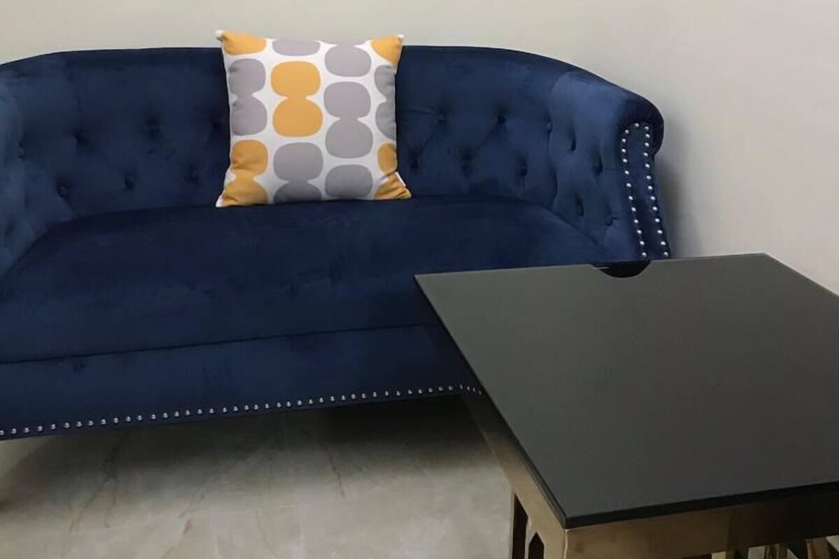 A blue sofa with a patterned pillow and a small wooden table with a black top.