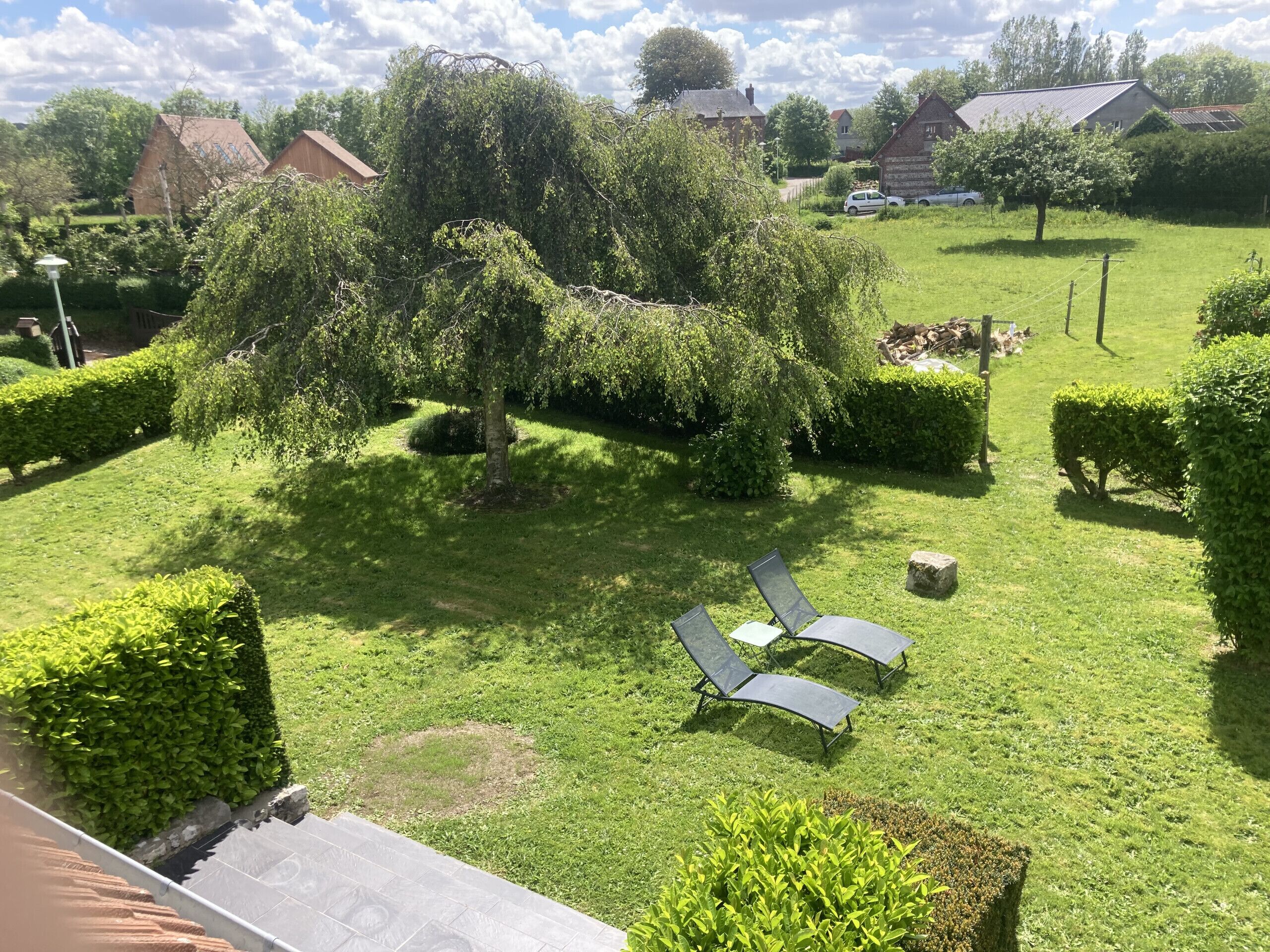 Ein gepflegter Garten mit geschnittenen Hecken, einer Rasenfläche und zwei Liegestühlen.