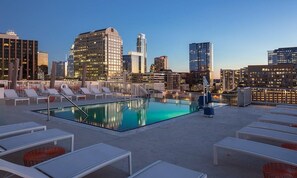 Ein Pool auf dem Dach mit Liegestühlen und einer Skyline im Hintergrund.