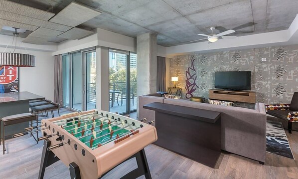 Ein modernes Wohnzimmer mit einer Fußballstoßmaschine, einer Couch, einem Fernseher und einem Balkon mit Sitzgelegenheit.