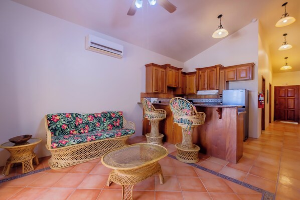 Una cocina con armarios de madera, un refrigerador y un comedor con mobiliario de mimbre.