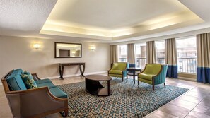 A hotel room with a sofa, armchairs, a small table, a mirror, and a view of the outside.