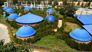 A view of a resort with multiple dome-shaped buildings, a swimming pool, and a fenced garden area. - Gumbaz Eco SPA Hotel (Samarkand)