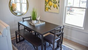 Un coin repas avec une table en bois foncé, quatre chaises, un miroir rond et un tableau représentant des citrons accroché au mur.