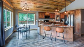 Une cuisine moderne avec des meubles en bois, un îlot central doté de tabourets de bar et une grande fenêtre qui laisse entrer la lumière naturelle.