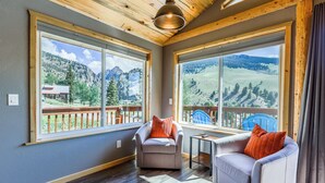 Une pièce chaleureuse avec deux canapés placés face à de grandes fenêtres, des poutres en bois au plafond et une vue sur un paysage montagneux.