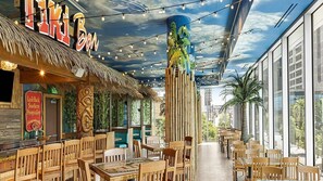 An indoor restaurant with wooden furniture, a thatched roof, and a mural on the ceiling.