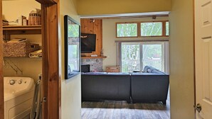 A compact kitchen with a stone fireplace, wooden cabinets, and a large window overlooking a deck.