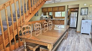 A dining area with a wooden table and chairs, a wooden staircase, and a kitchen in the background.