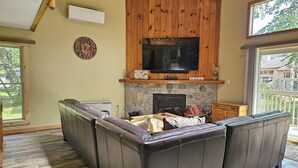 A living room with a stone fireplace, a large flat-screen TV, and a wooden ceiling.