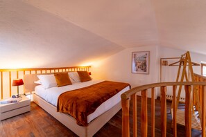 Un dormitorio con cama de madera, una mesita de noche, una lámpara, un cuadro enmarcado en la pared y una escalera de madera.