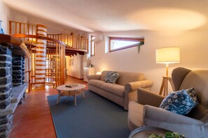 Una sala de estar acogedora con chimenea, una escalera en espiral de madera, un sofá y una lámpara.