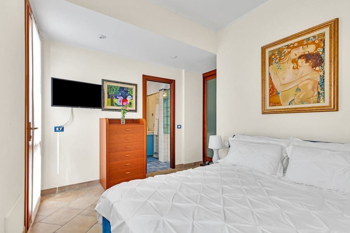 Une chambre d’hôtel avec un lit, une télévision, un tableau et une salle de bain visible à travers une porte ouverte.