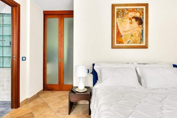 A hotel room with a bed, a nightstand, a lamp, a painting, and a sliding door.