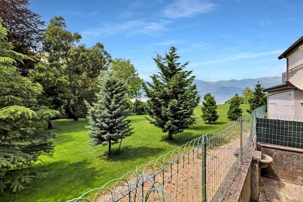 A fenced garden with various trees and a building in the background.