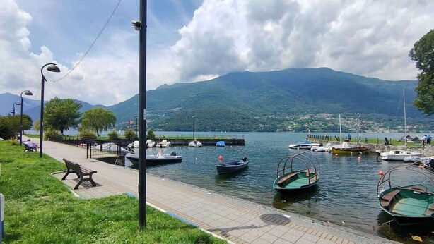 A lakeside walkway with boats, a bench, and a distant mountain.