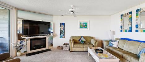 A living room with a fireplace, a television, a sofa, a coffee table, and a ceiling fan.
