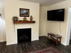 Ein Wohnzimmer mit Kamin, einem Wand-Fernseher und einem Holzboden mit Dekorationen.