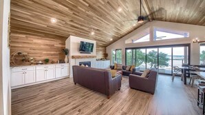A spacious living area with a high ceiling, wooden flooring, and large windows offering a view of the outdoors. - CL 874 Million Dollar View. Lake is now 100% full! (Canyon Lake)