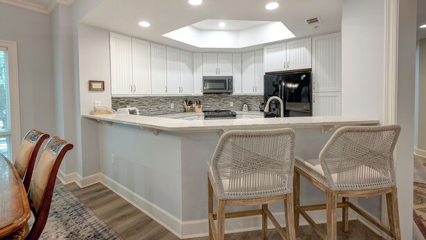 Una cocina moderna con armarios blancos, una isla central y dos taburetes de mimbre.