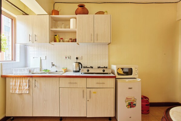 A kitchen with light wooden cabinets, a white countertop, a stove, a microwave, and a refrigerator.