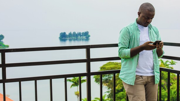 A person standing on a balcony with a railing, looking at a smartphone.
