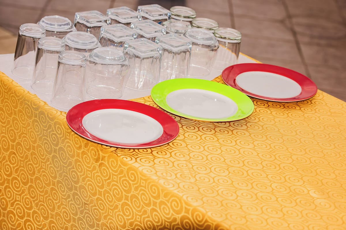 Une table avec des bocaux en verre transparent et des assiettes colorées, le tout posé sur une nappe à motifs.