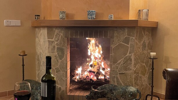 Un caminetto con rivestimento in pietra, una bottiglia di vino e un bicchiere di vino rosso su un pavimento piastrellato.