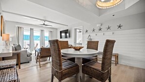 Een moderne eethoek met rieten stoelen, een ronde witte tafel en een plafondventilator.