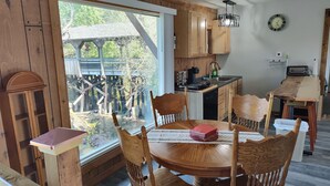Un intérieur rustique en bois comprenant un coin repas, une cuisine et une grande fenêtre donnant sur une terrasse en bois.