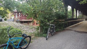 Un pont en bois, à ciel ouvert, avec un chemin de gravier menant à un bâtiment à la façade rouge.