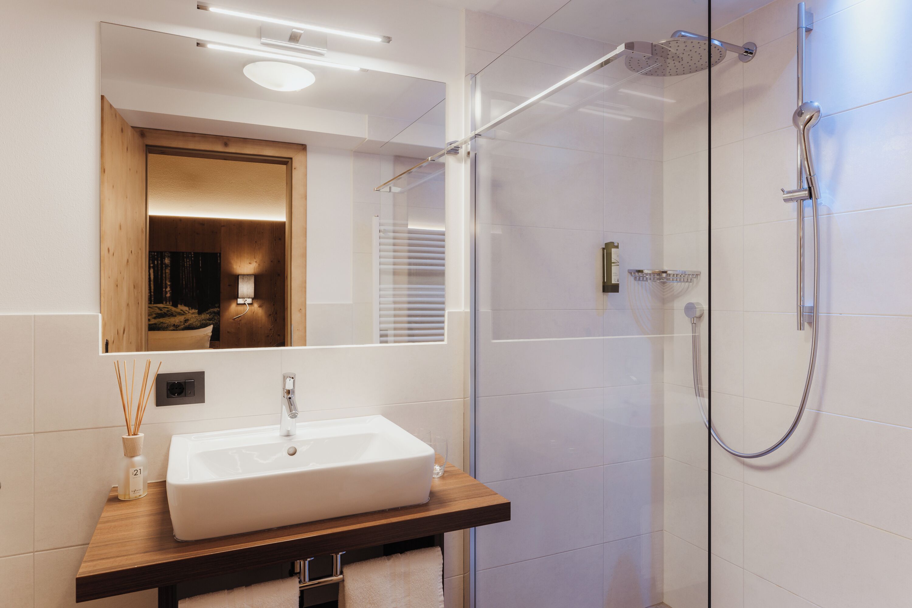 Une salle de bain moderne avec un grand miroir, un lavabo blanc et une douche à parois de verre.
