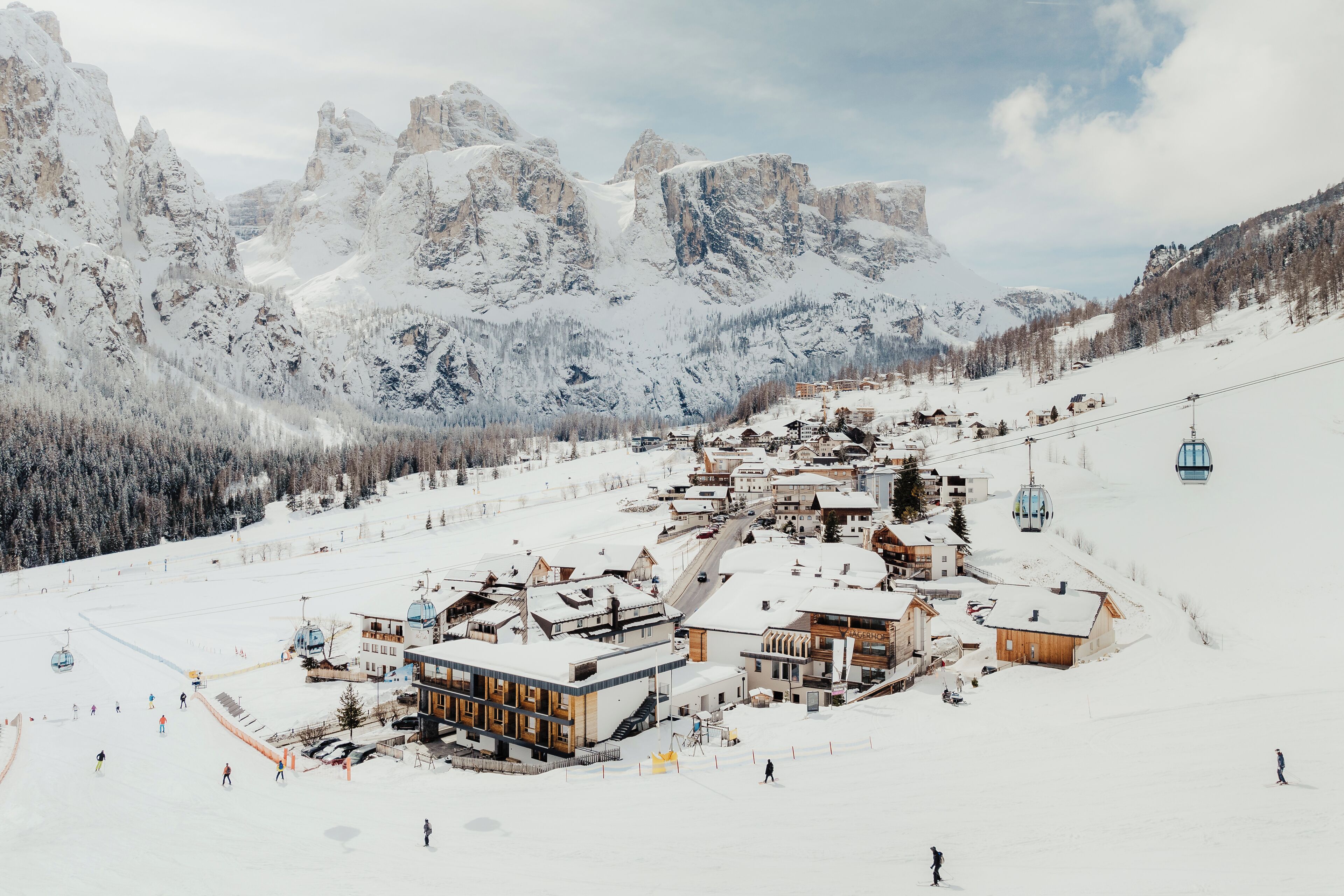 Una stazione sciistica innevata con edifici, una seggiovia e montagne sullo sfondo.
