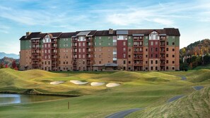 A multi-story hotel with a green and brown facade, located on a golf course with bunkers and a pond. - 1br Deluxe Pool View Unit with Waterpark! (Sevierville)