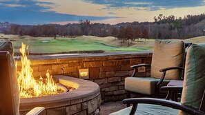 A stone fire pit with chairs, a view of a golf course, and a stone wall. - 1br Deluxe Pool View Unit with Waterpark! (Sevierville)