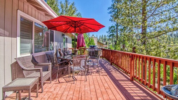 A wooden deck with outdoor furniture and a red umbrella, surrounded by trees. - Skyridge Cabin at Pine Mountain Lake (Groveland)
