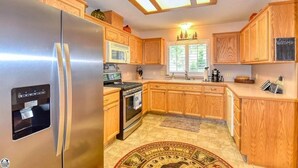 A kitchen with wooden cabinets, a stainless steel refrigerator, a microwave, a stove, and a window with a view of trees. - Skyridge Cabin at Pine Mountain Lake (Groveland)