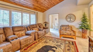 A spacious living room with a high wooden ceiling, a large leather sofa, a patterned armchair, and a decorative rug. - Skyridge Cabin at Pine Mountain Lake (Groveland)