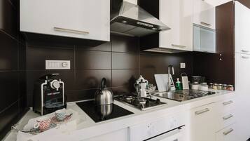 A modern kitchen with white cabinets, a black stove, a coffee machine, and a kettle.