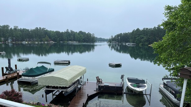 Un lac où des bateaux sont amarrés à un quai en bois, entouré d’arbres et d’une zone herbeuse.