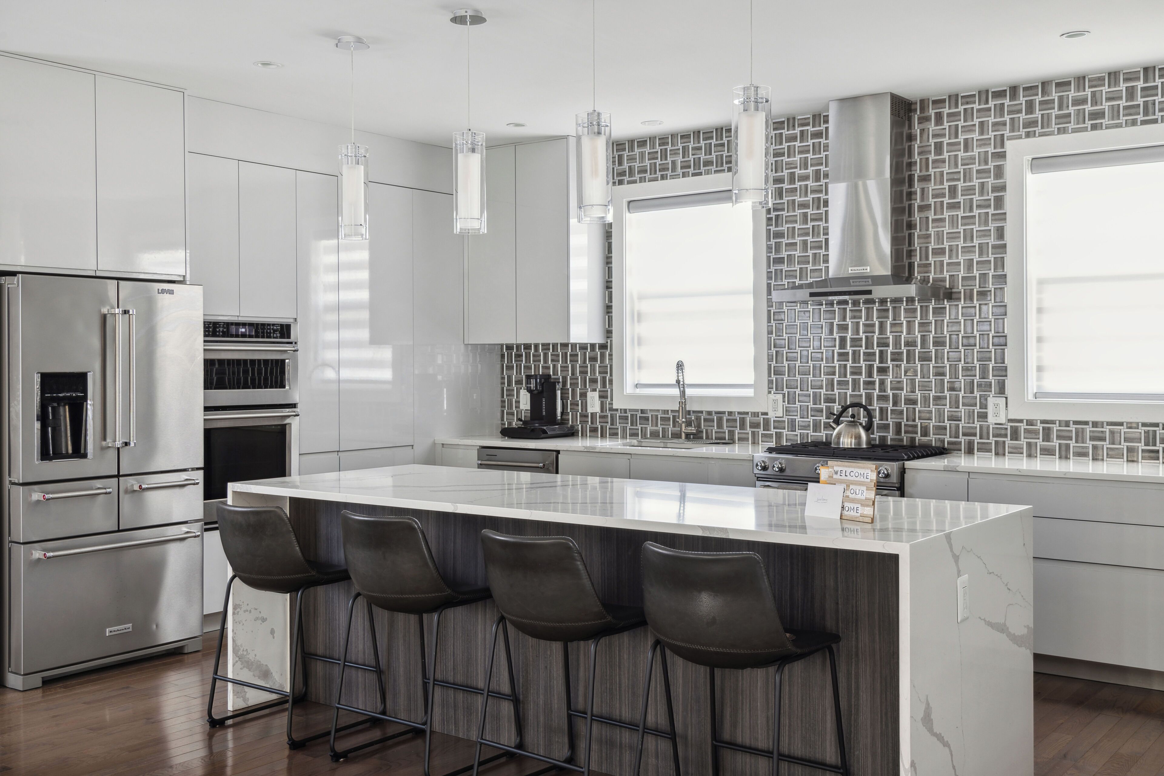 A modern kitchen with stainless steel appliances, a marble island with bar stools, and a backsplash of gray tiles.