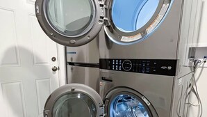 Un appareil combiné lave-linge et sèche-linge à chargement frontal, doté d’un panneau de commande, installé dans une pièce dont le sol est carrelé et qui possède une porte blanche.