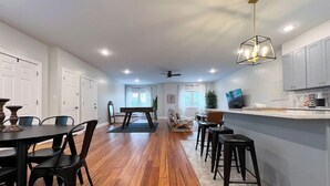 Une cuisine spacieuse avec un plancher en bois, un coin repas avec une table et des chaises, et un bar avec des tabourets.