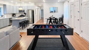 Une cuisine moderne avec un baby-foot, des meubles gris et un coin repas comprenant une table et des chaises.