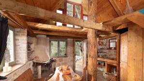 Un intérieur rustique avec des éléments en bois, une cheminée en pierre, des poutres apparentes et un coin repas comprenant une table et des chaises.